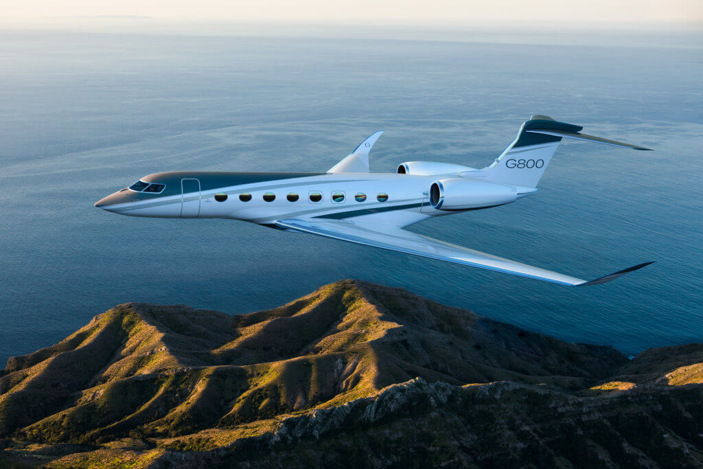 Gulfstream G800 private jet in flight over sea and green mountainous hills 